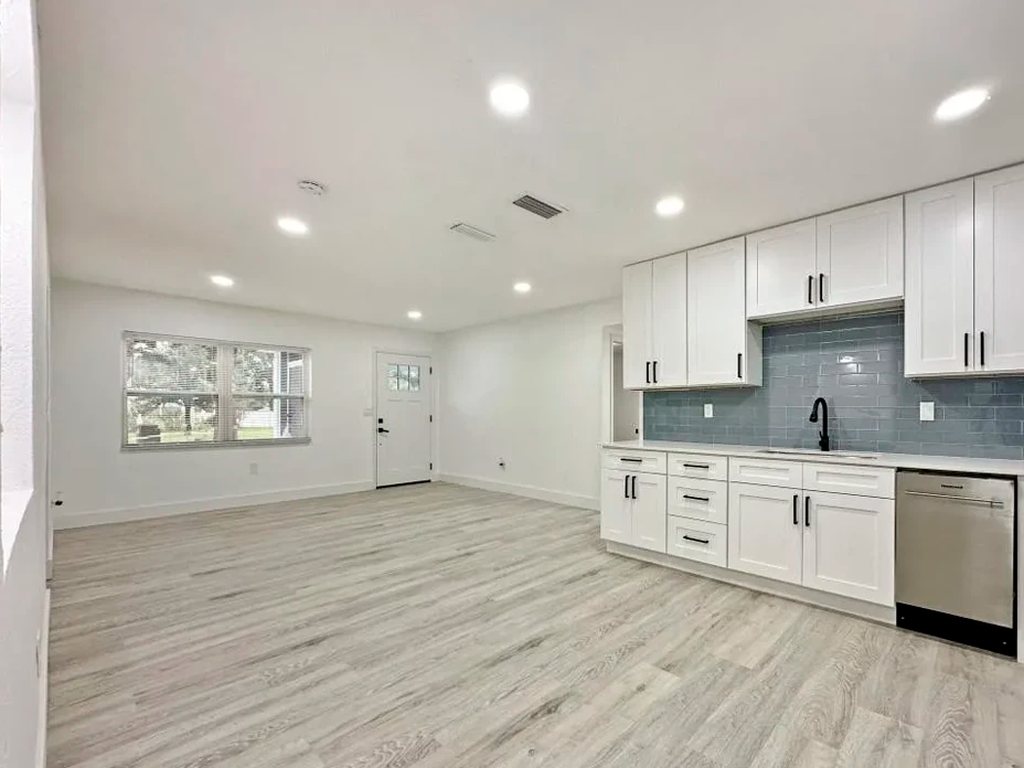 A finished kitchen remodel with white shaker cabinets, blue glass tile and recessed lighting